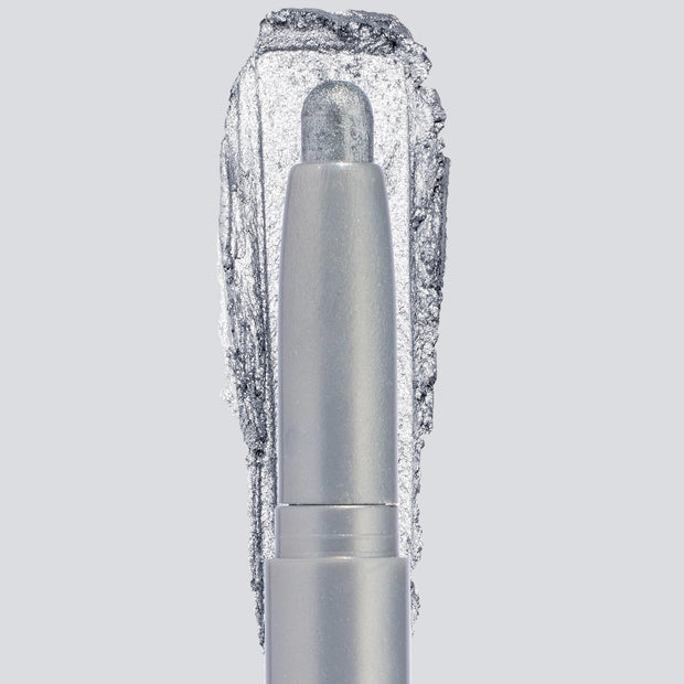 ColourPop Shadow Stix in Witch, Please showcases a creamy icy-silver shimmer, the crayon tip extended with a bold swatch behind to highlight pigment and sparkle, centered in a sleek silver tube on a light gray background.