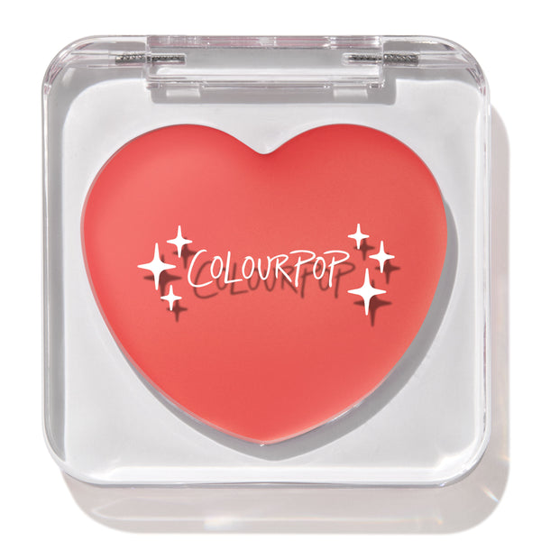 Heart-shaped Baby Bunny ColourPop Lip and Cheek Balm shown closed in a clear square compact, coral-pink tint with white sparkle graphics and ColourPop logo, displayed under studio light on a white background.