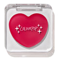 Heart-shaped hot pink compact with white “ColourPop” logo and sparkles rests closed in a clear square case, featuring the ColourPop Lip and Cheek Balm in Girls Night, a rosy multitasking balm for lips and cheeks.