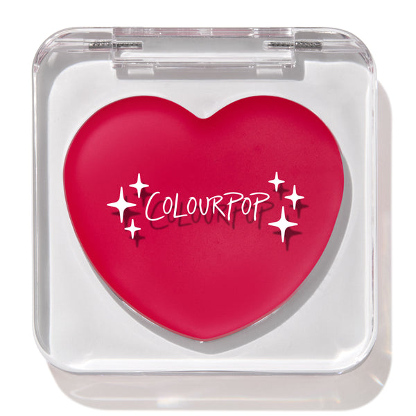 Heart-shaped hot pink compact with white “ColourPop” logo and sparkles rests closed in a clear square case, featuring the ColourPop Lip and Cheek Balm in Girls Night, a rosy multitasking balm for lips and cheeks.