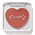 Heart-shaped ColourPop Lip and Cheek Balm in Larchmont Village sits closed in a clear square compact with sparkles logo, showcasing a warm terracotta hue on a bright white background.