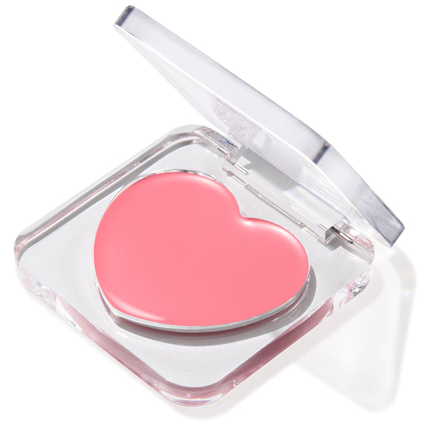 Heart-shaped soft pink Lucky U Lip and Cheek Balm set in a clear acrylic compact with the lid half open, creamy finish catching light against a white backdrop; ColourPop Lip and Cheek Balm.
