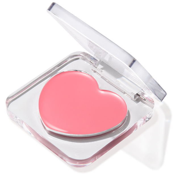 Heart-shaped soft pink Lucky U Lip and Cheek Balm set in a clear acrylic compact with the lid half open, creamy finish catching light against a white backdrop; ColourPop Lip and Cheek Balm.