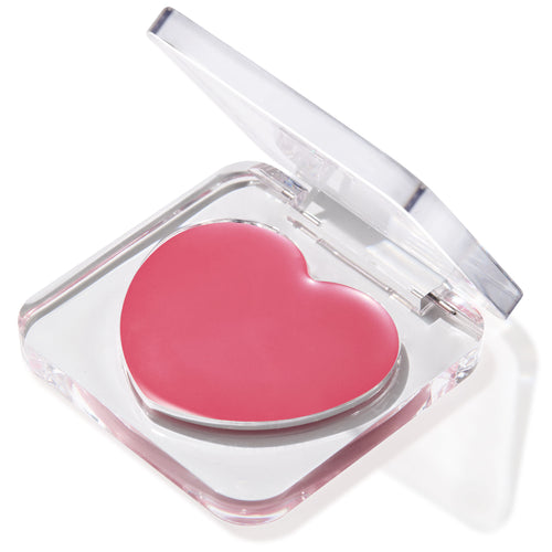 Heart-shaped pink balm in the Verified shade sits in a half-open clear compact, glossy pan catching light on a white background; multitasking ColourPop Lip and Cheek Balm for buildable tint on lips and cheeks.