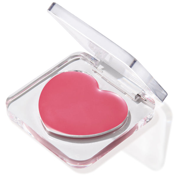 Heart-shaped pink balm in the Verified shade sits in a half-open clear compact, glossy pan catching light on a white background; multitasking ColourPop Lip and Cheek Balm for buildable tint on lips and cheeks.