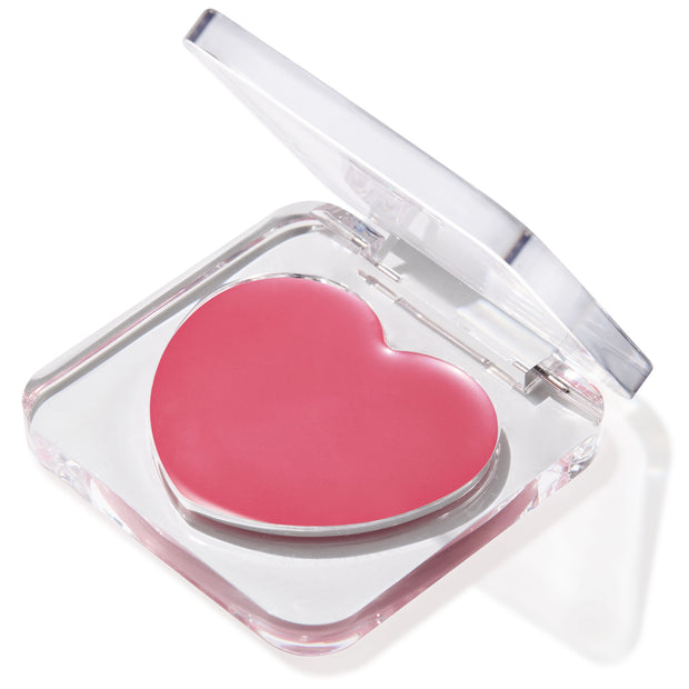 Heart-shaped pink balm in the Verified shade sits in a half-open clear compact, glossy pan catching light on a white background; multitasking ColourPop Lip and Cheek Balm for buildable tint on lips and cheeks.