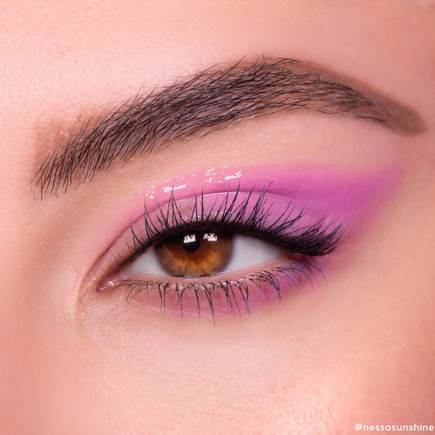 Brown eye wears In The Clear Face & Eye Gloss, creating a glassy wet-look over pink‑lavender shadow; fluttery lashes and a defined brow frame the lid, showcasing ColourPop Face & Eye Gloss shine in a macro beauty close-up.