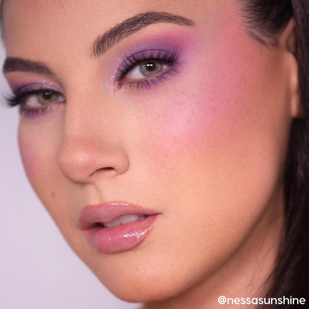 Hypnosis ColourPop Cream Blush sweeps a soft cool-pink flush across the model’s cheek, shown in a tight beauty close-up with lavender shimmer eyeshadow, full lashes, and glossy nude lips in studio lighting.
