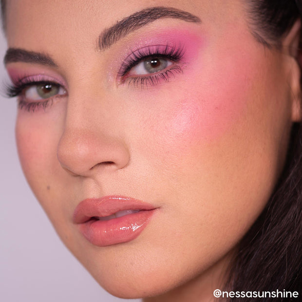 Metronome ColourPop Cream Blush adds a dewy hot‑pink flush on the model’s cheek, blending toward the temple; close-up shows soft pink eyeshadow, full lashes, and glossy nude lips under studio lighting.