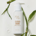 Cloud Bank Milky Cleanser bottle by Fourth Ray Beauty rests on a glossy, milk-like surface with water droplets, framed by green bamboo leaves; white pump-top 5.8 fl oz (171 ml) packaging, presented as a gentle ColourPop Face Cleanser.