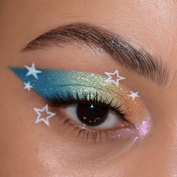 White Graceland BFF Liquid Liner tracing crisp star accents around a brown eye over a teal-to-gold-to-peach shimmer wing; ColourPop BFF Liquid Liner defines the graphic look beneath natural lashes and a neatly groomed brow.