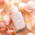 Rose Face Milk bottle by Fourth Ray Beauty resting among soft pink rose petals, a pale pink 0.95 fl oz (28 ml) dropper serum on a blush background; hydrating ColourPop Face Milk skincare product highlighted in a delicate floral setting.