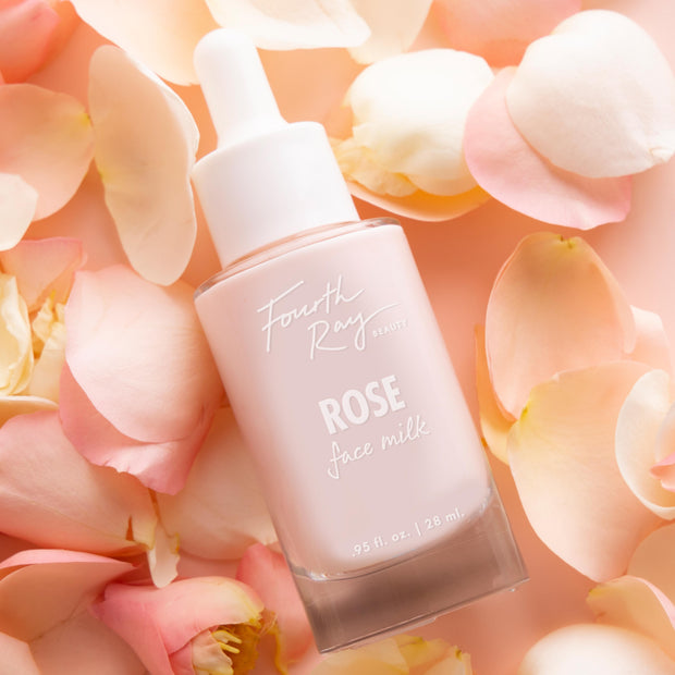 Rose Face Milk bottle by Fourth Ray Beauty resting among soft pink rose petals, a pale pink 0.95 fl oz (28 ml) dropper serum on a blush background; hydrating ColourPop Face Milk skincare product highlighted in a delicate floral setting.