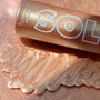 Rosè SOL Glow Oil bottle resting on a rose-gold surface, with a zigzag swatch of pearly rose shimmer showing its luminous finish; ColourPop SOL Glow Oil body highlighter in shade Rosè for a sun-kissed glow.