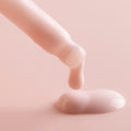 Dropper dispenses a creamy, pale-pink Rose Face Milk, forming a glossy droplet on a soft blush background, showcasing the ColourPop Face Milk serum in a minimal macro product shot.