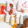 Watermelon Face Milk bottle with dropper stands center-left, labeled Fourth Ray, surrounded by fresh watermelon slices, strawberries, rose petals, oats, turmeric, coconut, and sister variants - a ColourPop Face Milk skincare flat lay for dewy hydration.
