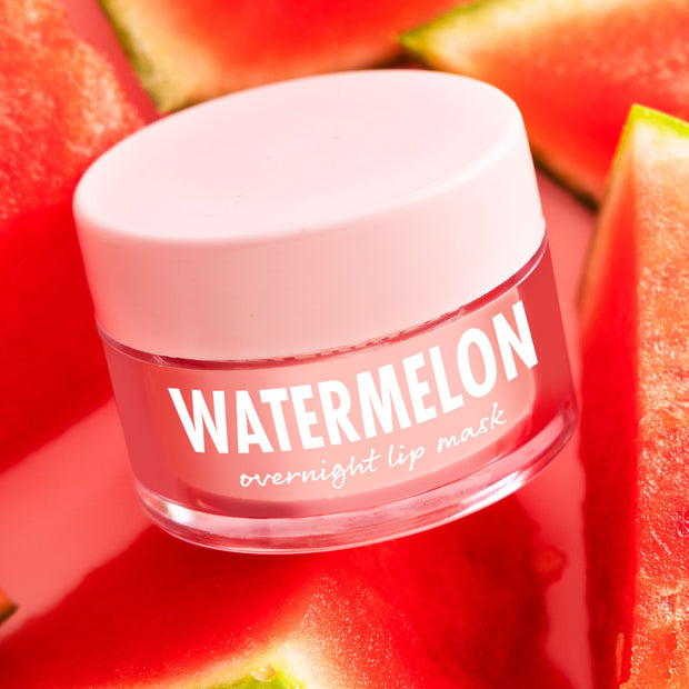 ColourPop Watermelon Lip Mask jar with pale pink lid and clear glass, labeled “Watermelon overnight lip mask,” resting among fresh watermelon slices on a bright pink backdrop, showcasing a hydrating overnight treatment.