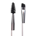 ColourPop Brow Dual Ended Brush makeup brush shaping and defining eyebrows, featuring a black spoolie on one end and an angled flat brush on the other with silver ferrules and a white handle, shown in a studio close-up on a white background.