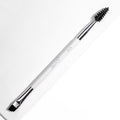 ColourPop Brow Dual Ended makeup brush resting diagonally, featuring an angled flat brow brush for filling and a black spoolie for grooming, white handle with chrome ferrules, on a bright white textured background.