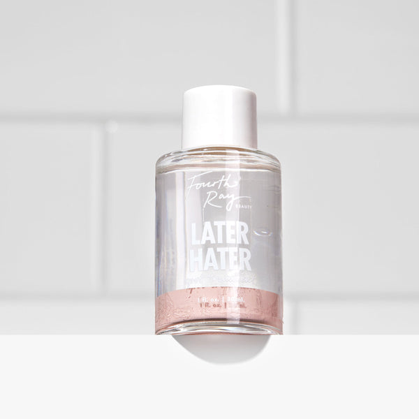 Fourth Ray Beauty Later Hater Spot Treatment bottle standing upright, showing clear liquid with pink sediment at the base and a white cap, on a white bathroom shelf against glossy subway tiles; ColourPop acne face treatment product.