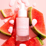 Pink dropper bottle of Fourth Ray Beauty Watermelon Face Milk standing amid fresh watermelon slices, creamy pink formula dripped on a blush background; a hydrating 0.95 fl oz ColourPop Face Milk with a juicy, summery skincare vibe.