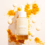 Fourth Ray Beauty Turmeric Face Milk dropper bottle with white cap stands upright, 0.95 fl oz/28 mL, filled with pale yellow serum, surrounded by creamy droplets and bright orange turmeric powder on a light backdrop, featuring ColourPop Face Milk skincare.
