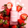 Pink glass dropper bottle of Fourth Ray Beauty Strawberry Face Milk (0.95 fl oz/28 ml) standing amid sliced strawberries and milky droplets on a blush backdrop, highlighting a hydrating ColourPop Face Milk serum.