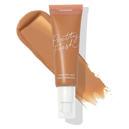 ColourPop Pretty Fresh Tinted Moisturizer in Medium Dark 15 W, a tan tube with white pump and blush pink cap labeled Pretty Fresh and hyaluronic acid, angled over a warm medium-dark shade swatch on a white background.