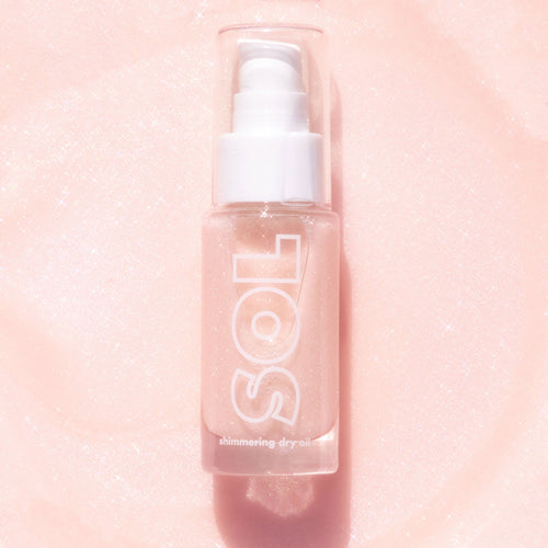 ColourPop SOL Shimmering Dry Oil in Soft Pink stands upright in a clear bottle with white pump and cap, fine shimmer suspended, SOL logo visible, catching light on a sparkly blush-pink background.