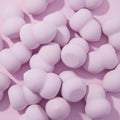 Hourglass Blending Sponge, lavender hourglass-shaped beauty sponges scattered on a pastel pink surface, featuring a double-curved design for smooth foundation and concealer blending; pairs well with ColourPop Makeup Tools & Accessories.