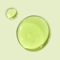 Avocado + Aloe Double Shot face serum forming glossy, translucent green drops that pool on a pale mint background, highlighting a lightweight, hydrating texture; ColourPop Face Serum.