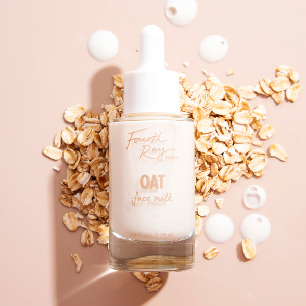 Fourth Ray Beauty Oat Face Milk dropper bottle standing amid oat flakes, with milky serum drops on a nude background; hydrating ColourPop Face Milk highlights a gentle oat formula and creamy texture for soothing skincare.