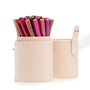 ColourPop Small Stash Cup holding assorted pink and nude makeup pencils, a two-piece cylindrical brush holder with snap strap and embossed logo in pale beige, ideal makeup tools & accessories organizer on a white background.