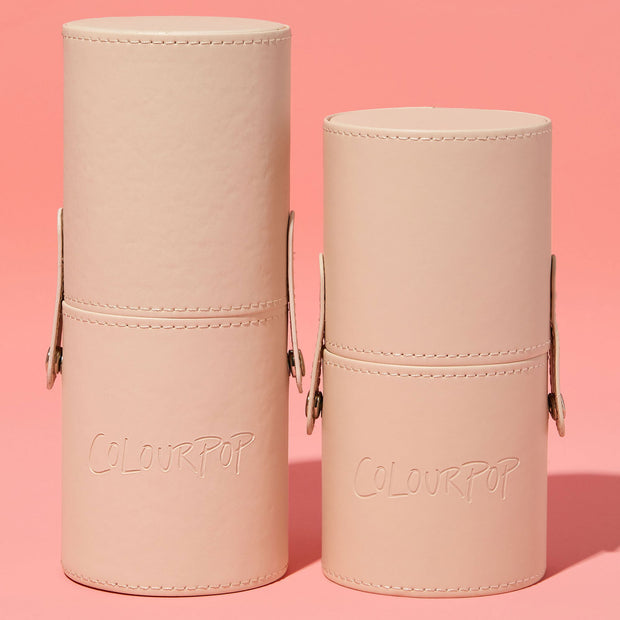 ColourPop Small Stash Cup standing upright - two nude, faux-leather cylindrical holders with snap side straps, stitched trim, and embossed logo - organizing makeup tools and accessories, shown side by side on a pink backdrop.