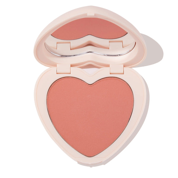 ColourPop Kiss 'N Tell pressed powder blush compact, open to reveal a peachy-rose heart-shaped pan and heart mirror, in pale pink packaging on a white background.