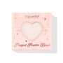 ColourPop Kiss 'N Tell pressed powder blush compact displays through a heart-shaped window in a pink box with winged-heart graphics, front-facing on a white background, 4.45g (0.16 oz) makeup packaging for US shoppers.
