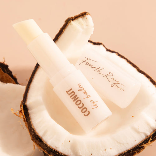 Coconut Lip Balm by Fourth Ray Beauty for ColourPop, tube uncapped to reveal creamy stick, nestled inside a halved coconut on a warm beige backdrop.