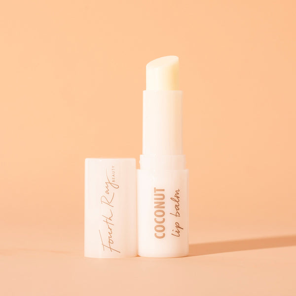 ColourPop Fourth Ray Beauty Coconut lip balm standing uncapped, creamy balm bullet exposed in a glossy white tube labeled COCONUT lip balm, cap beside it, on a warm peach background with soft shadow.