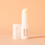 ColourPop Fourth Ray Beauty Coconut lip balm standing uncapped, creamy balm bullet exposed in a glossy white tube labeled COCONUT lip balm, cap beside it, on a warm peach background with soft shadow.
