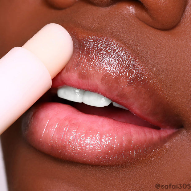 ColourPop Vanilla Lip Balm gliding across lips, delivering a glossy, moisturizing sheen; close-up shows a pale pink twist-up tube applying the sheer vanilla balm to smooth, soft lips.
