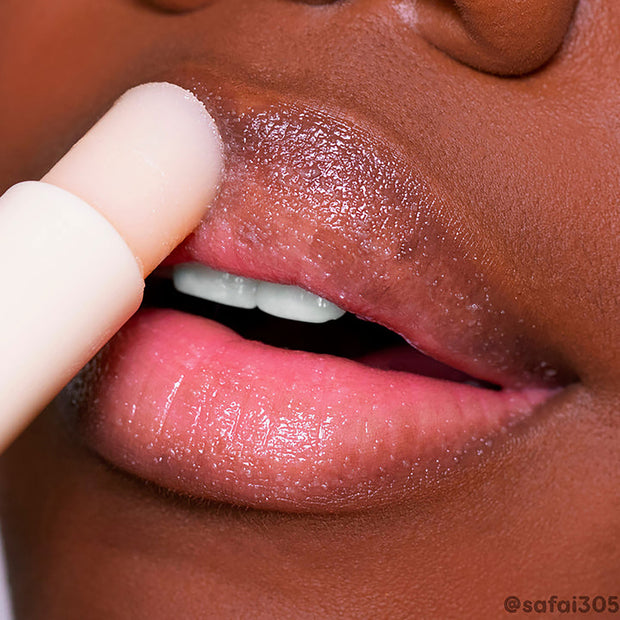 ColourPop Vanilla Lip Scrub stick exfoliating dry lips in a close-up, creamy vanilla balm gliding over the upper lip to buff flakes and reveal a glossy, hydrated finish, with the nude twist-up applicator shown in use.