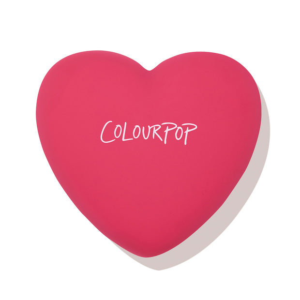 Heart-shaped hot pink compact with white ColourPop logo, closed and casting a soft shadow, featuring the Text Me shade of ColourPop Pressed Powder Blush; sleek travel-friendly pressed powder blush on a clean white background.