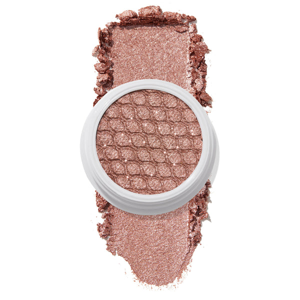Aster ColourPop Super Shock Shadow sits open in a white pot, honeycomb-pressed pan glistening in a rose-gold metallic shimmer, with crushed pigment swatched above and below on a clean white background.