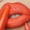 Chi Chi ColourPop Lippie Stix gliding onto lips, delivering bold tangerine-orange color while a matching lip pencil defines the edges, close-up beauty shot showing a smooth satin-matte finish.