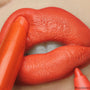 Chi Chi ColourPop Lippie Stix gliding onto lips, delivering bold tangerine-orange color while a matching lip pencil defines the edges, close-up beauty shot showing a smooth satin-matte finish.