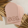SOL Body Tanning Mitt stacked on a second in soft pink, lying on neutral stone with dried palm fronds; plush, reusable applicator for even self-tanner application - an essential from ColourPop Makeup Tools & Accessories.
