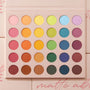 Matte About Hue ColourPop Shadow Palette displays 30 matte rainbow shadows - pink, orange, yellow, green, blue, purple, and neutrals - arranged in five rows of round pans, opened in a blush-pink case with printed shade names on a soft pink background.