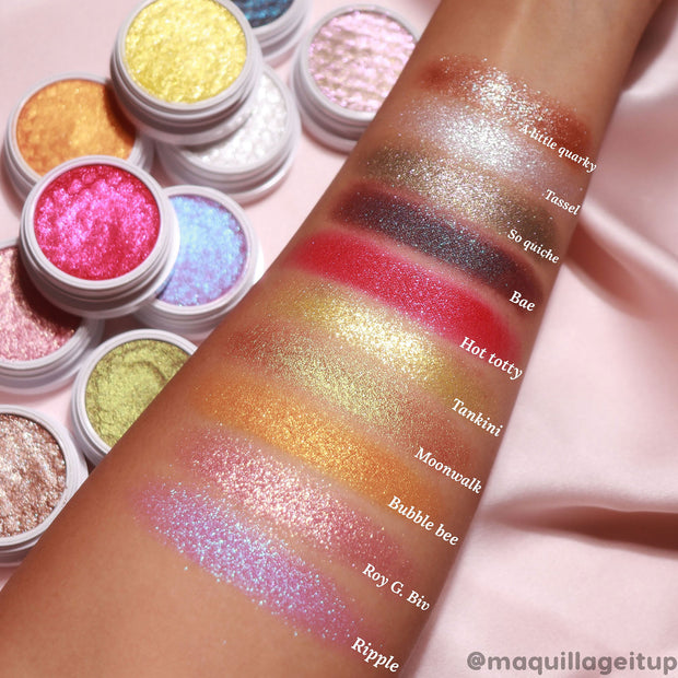 So Quiche Super Shock Shadow swatched on a forearm - shimmery olive-taupe with a green-gold shift - shown beside labeled swatches and open white pots of other ColourPop eyeshadows on a pink backdrop.