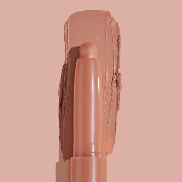 ColourPop Shadow Stix in Bare With Me smoothly swiped into a thick matte peachy-nude swatch, the crayon tip centered in close-up on a matching nude background, highlighting the creamy, long-wear eyeshadow stick.