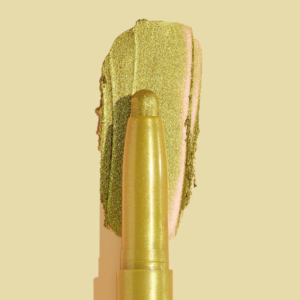 Flex ColourPop Shadow Stix depositing a metallic chartreuse-gold swipe on a beige background, showcasing creamy, blendable shimmer payoff and the twist-up pencil tip for quick eye shadow application.